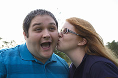 Photograph of a couple with girl kissing boy's cheek